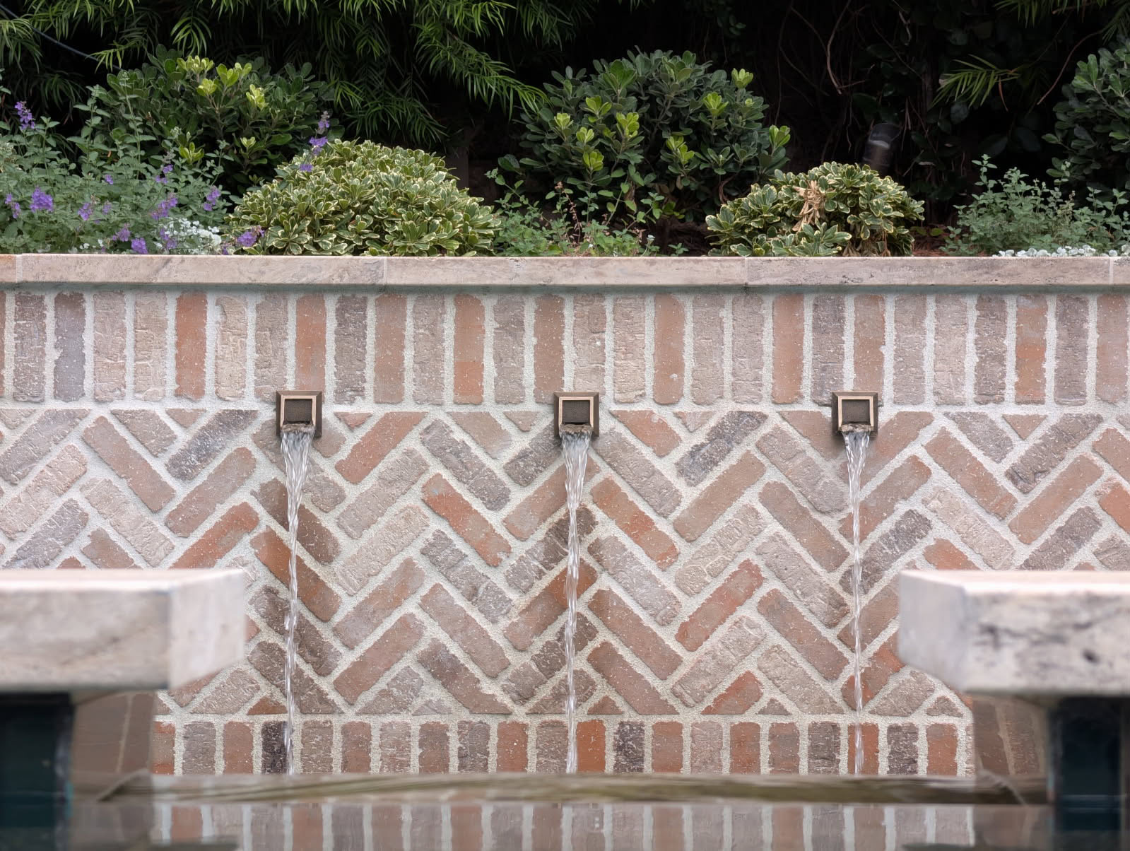 Herringbone brick wall with three scupper water features spilling into a pool