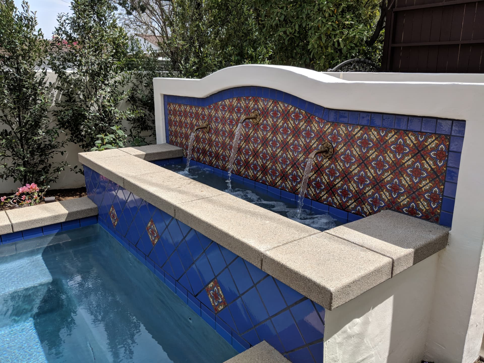 Cobalt tile fountain wall with three bronze scuppers pouring into a spa
